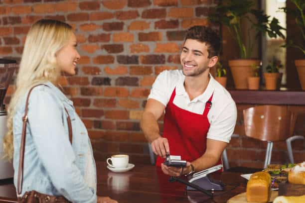 Serveur en tablier rouge accueillant une cliente dans un restaurant